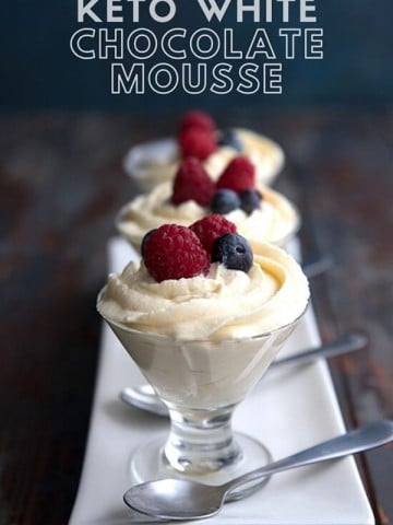 Titled Image: Three glass dessert cups filled with white chocolate mousse with berries on top, on a thin white platter.
