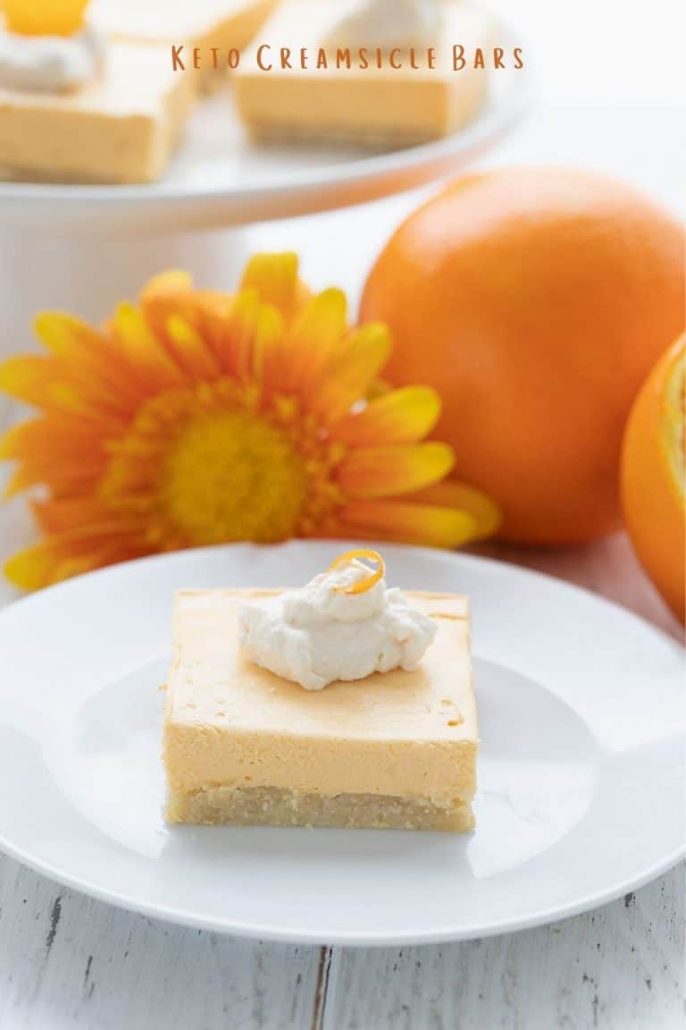 Titled image of a keto creamsicle on a white plate, in front of a cut up orange and some orange gerbera daisies