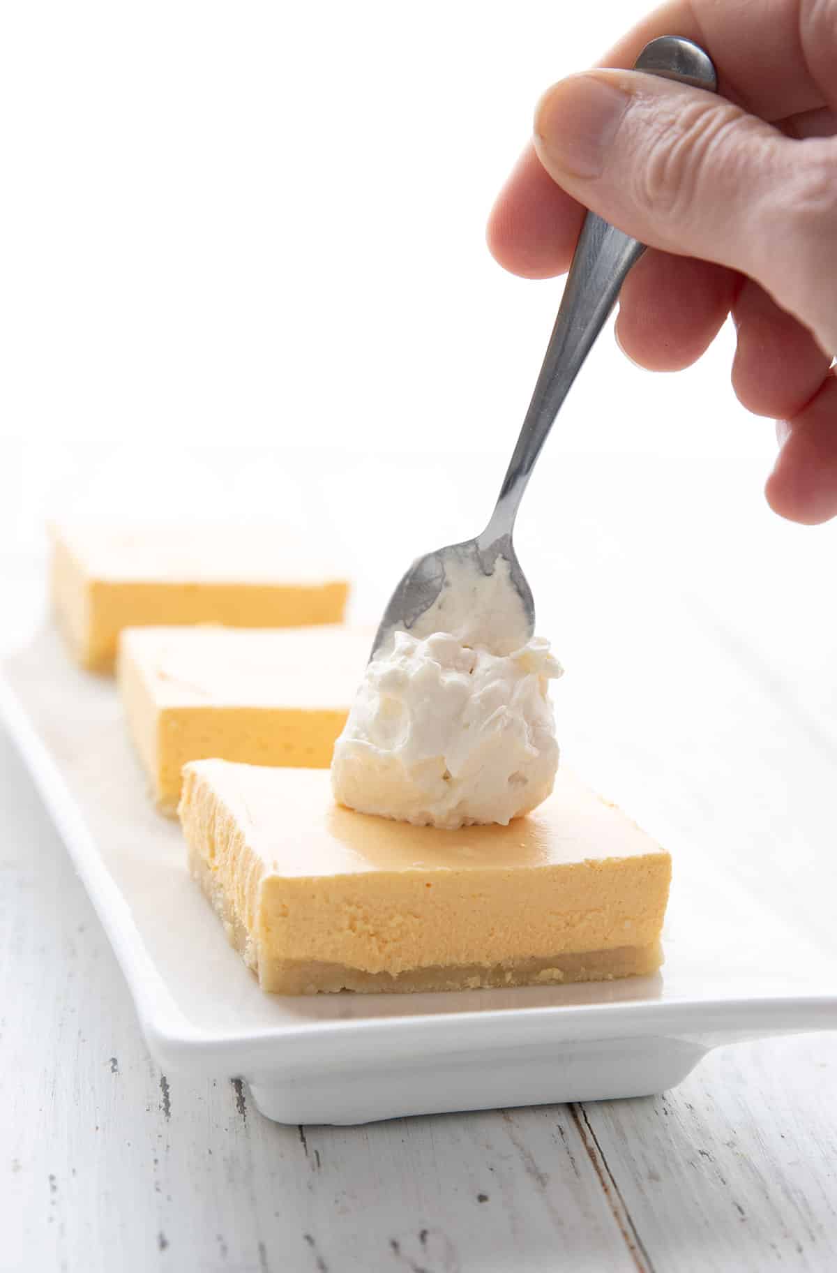 A spoon dolloping whipped cream on keto creamsicle cheesecake bars