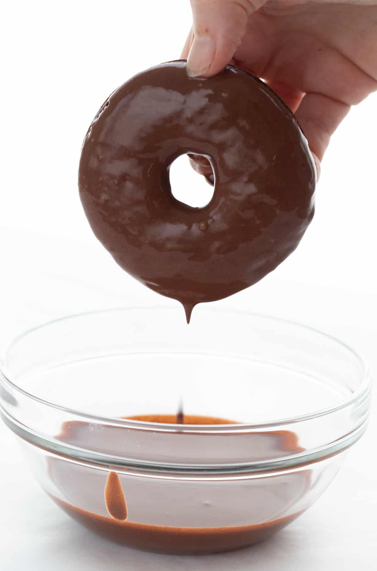 A hand holding a keto chocolate donut that has just been dipped in chocolate glaze. 