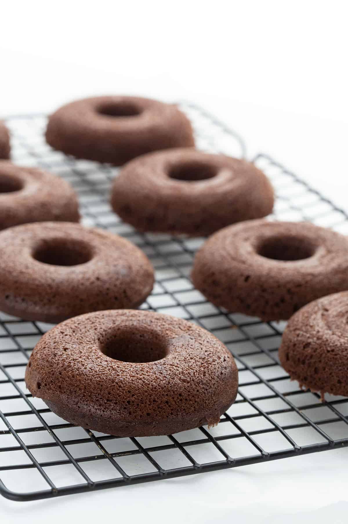 Keto chocolate donuts cooling on a rack over a white table. 