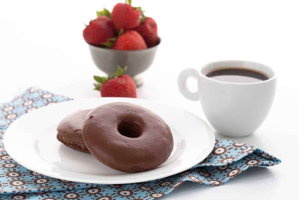 Keto chocolate donuts on a white plate with a cup of coffee and a bowl of strawberries