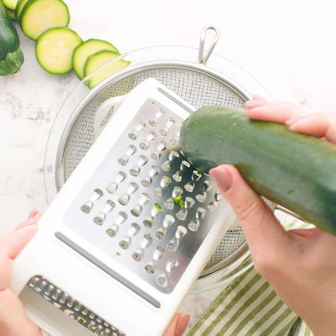 Zucchini being shredded on a box grater. 