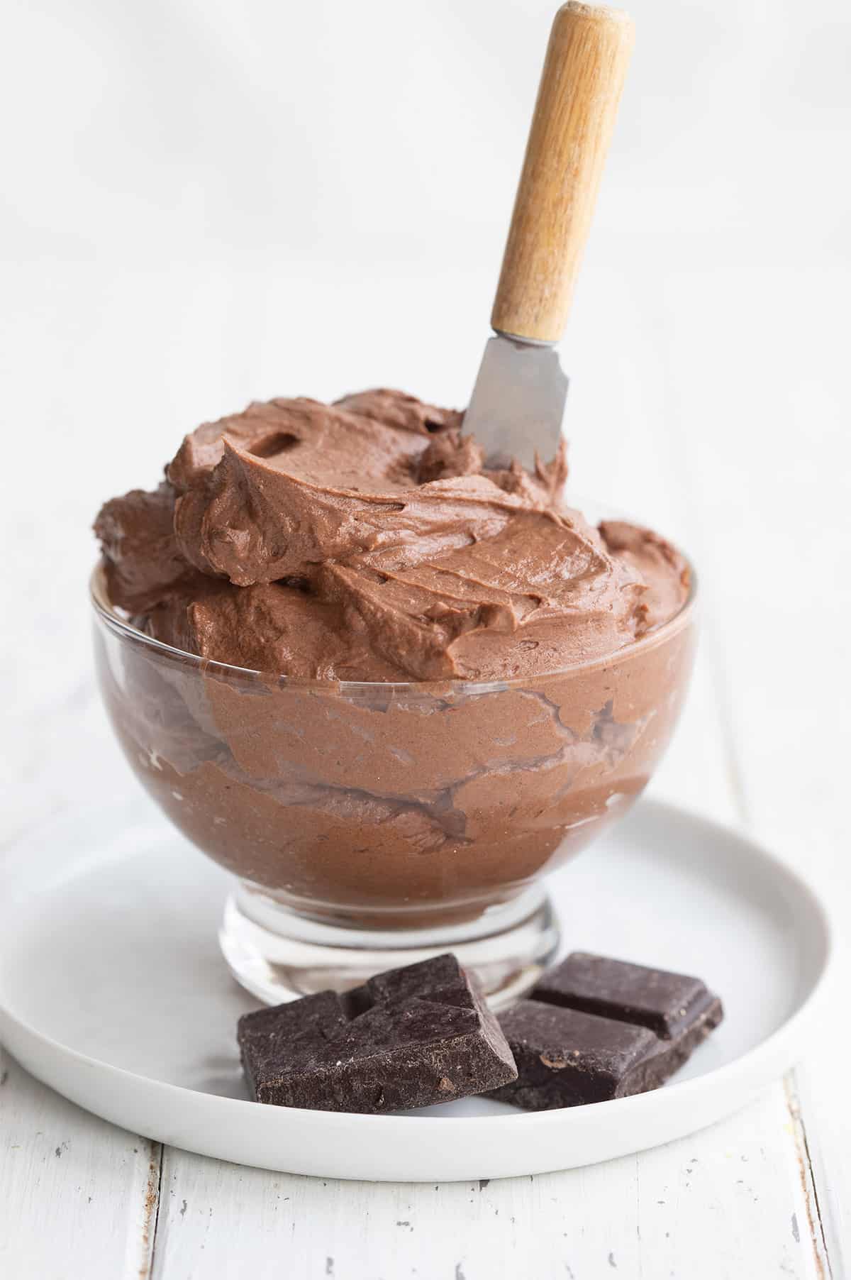 Keto chocolate frosting in a glass bowl with a small spreading knife stuck into it. 