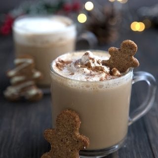 Two gingerbread lattes on a wooden table, with gingerbread men and Christmas lights.