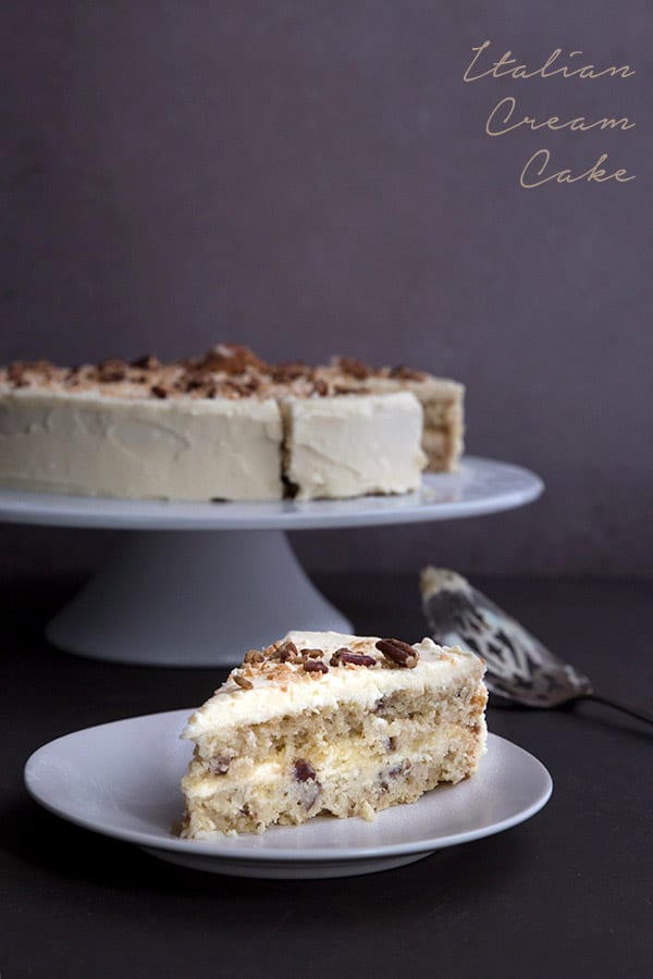 Keto Italian Cream Cake Recipe - a slice of cake on a white plate with the large cake in behind. 