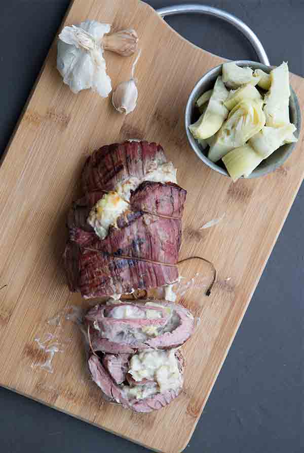 Low Carb Stuffed Flank Steak on a cutting board with artichokes and garlic