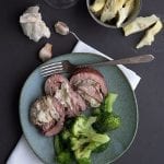 Keto artichoke stuffed flank steak on a plate with broccoli, along with a glass of wine.
