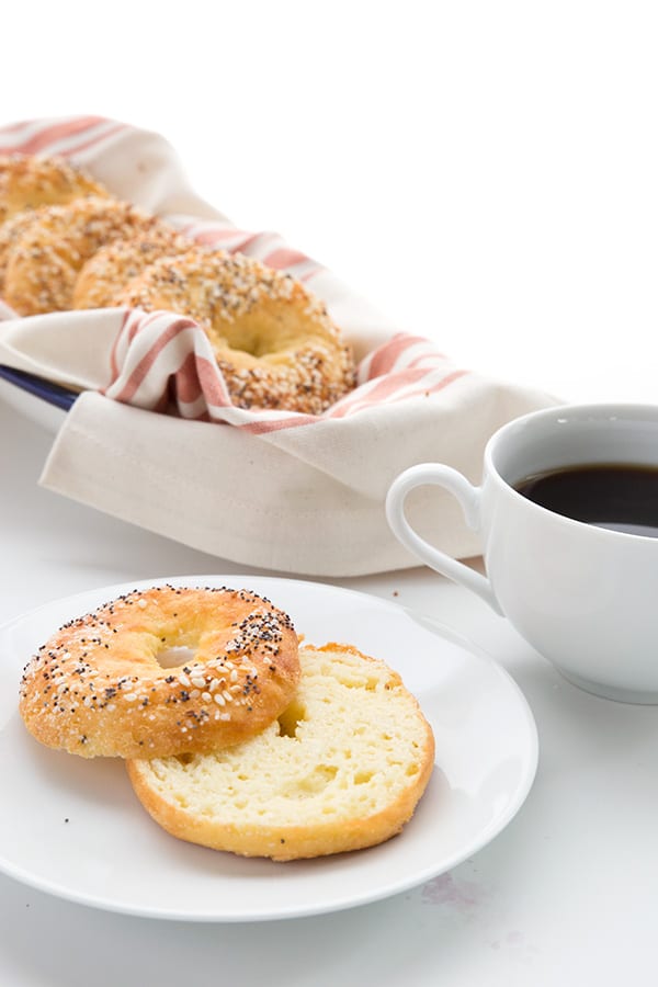 A sliced fathead dough bagel with more bagels in a bread basket and a cup of coffee