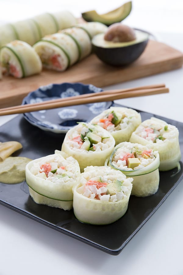Low carb cucumber and avocado sushi on a black platter with soy sauce and wasabi