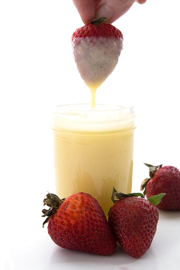 A strawberry being dipped into a jar of sweetened condensed milk