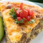 Close up shot of a slice of Taco Pie on a white plate with chopped tomatoes on top.