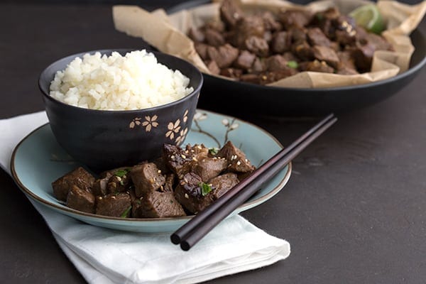 Steak bites on a plate with a bowl of cauliflower rice and some chopsticks