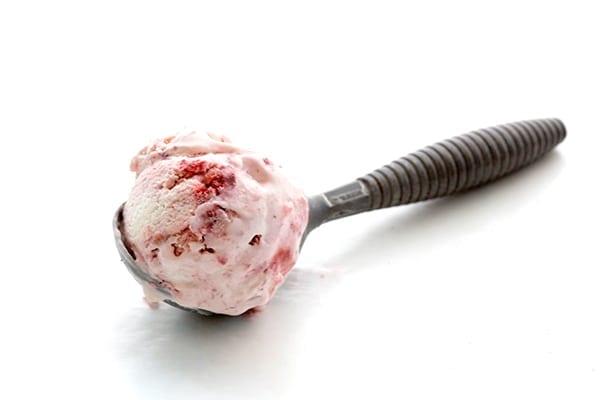 A scoop of low carb strawberry ice cream in an ice cream scoop on a white background