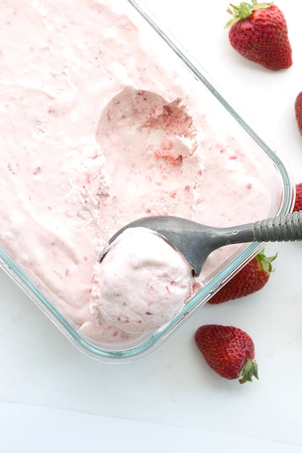 No Churn Strawberry Sour Cream Ice Cream in a glass container with a scoop and strawberries