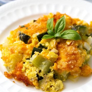A serving of Zucchini Casserole on a white dish with a sprig of basil on top.