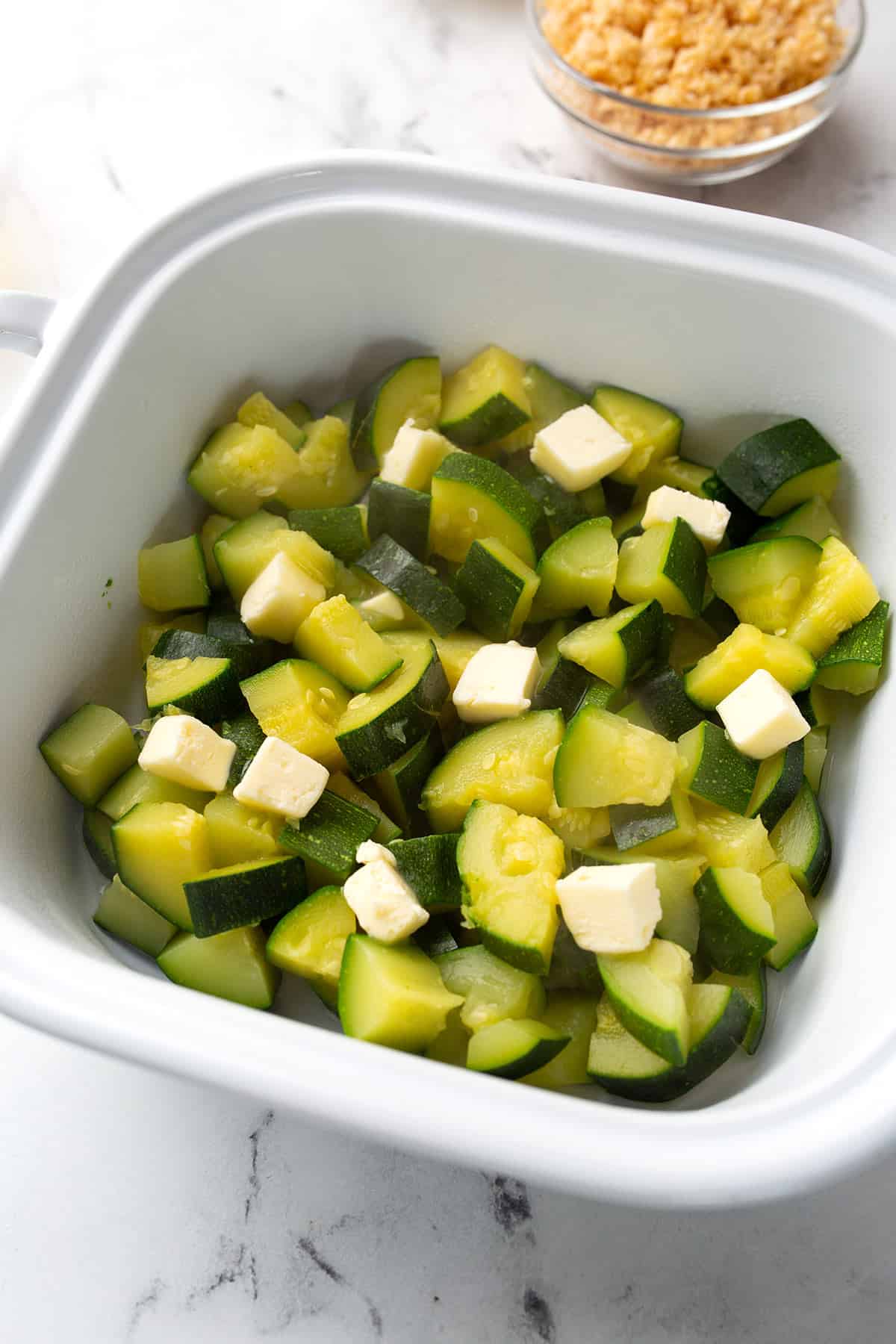 Blanched zucchini in a baking dish with butter dotted overtop. 