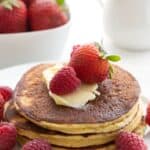 A stack of coconut flour pancakes on a white plate with fresh berries on top and all around.