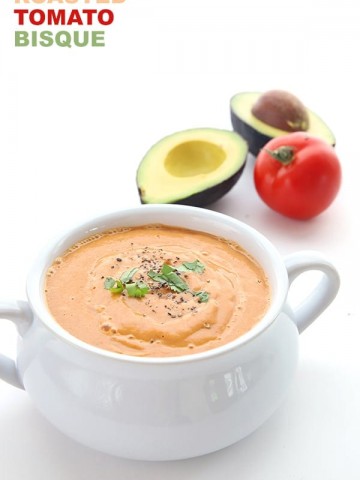 Dairy Free Low Carb Roasted Tomato Bisque in a white bowl with a tomato and avocado in the background