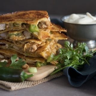 A stack of low carb chicken quesadillas with a bowl of sour cream behind