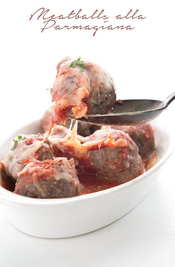 Meatball parmesan in a white oval dish with a spoon lifting one meatball away from the rest.