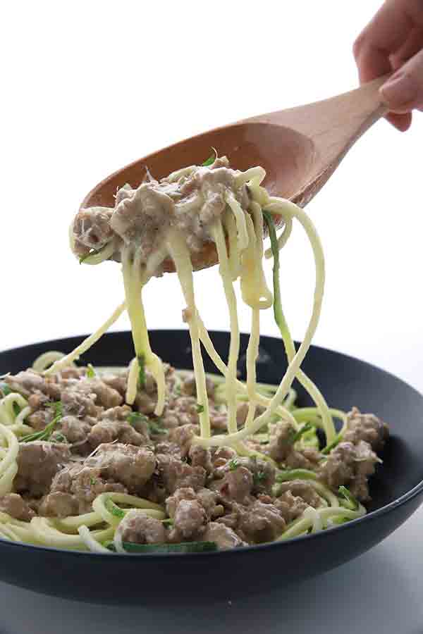 Sausage alfredo with zucchini noodles in a black bowl with a wooden spoon lifting some up