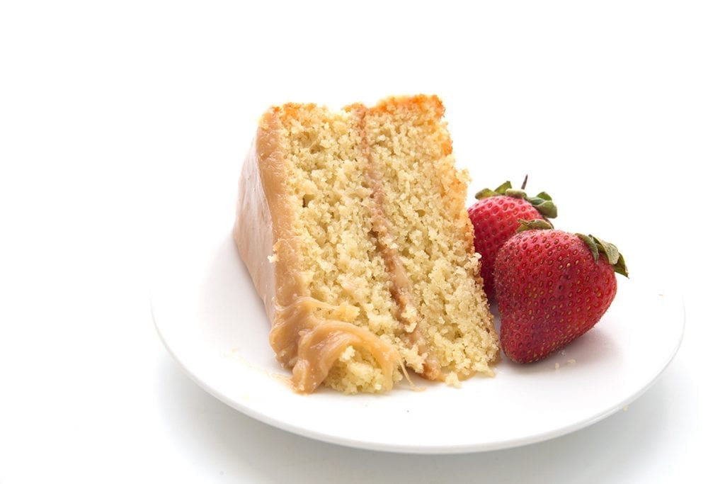 A slice of keto caramel cake a white plate with two strawberries