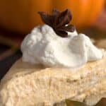 Titled image of a slice of keto pumpkin cream pie on a wooden table with a pumpkin in the background.