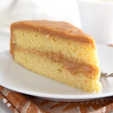 A slice of Keto Caramel Cake on a white plate over a patterned brown napkin.