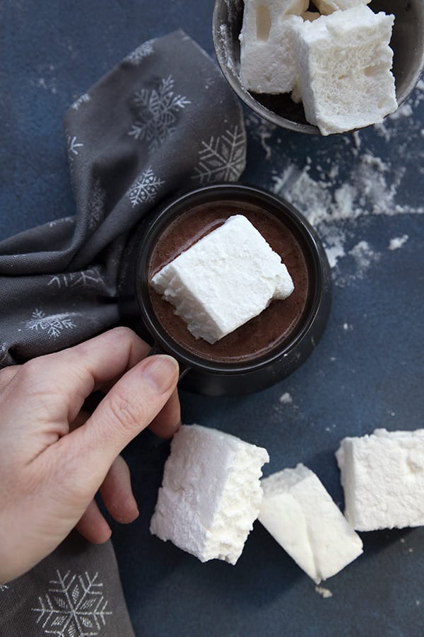 Hand on a mug of hot chocolate with a sugar free marshmallow floating in it. 