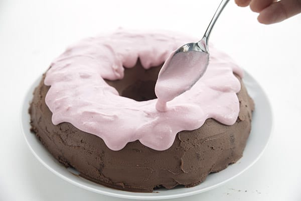 Spooning sugar free raspberry frosting over a keto donut cake.