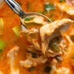 Close up shot of Keto Chicken Enchilada Soup in a white bowl, with a spoon lifting some up.