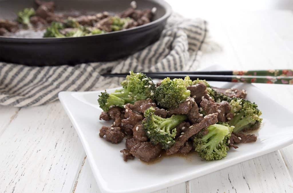 Keto sesame beef and broccoli on a white plate with chopsticks. 