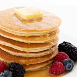 Titled image of a stack of keto pancakes on a white plate, with berries all around.