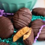 Titled image of Keto Peanut Butter Eggs on a wooden table with a teal bowl in the background.