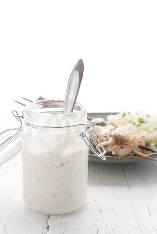 A jar of keto salad dressing with chicken souvlaki in the background