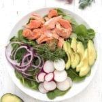 A large platter of spinach salad with salmon and avocado