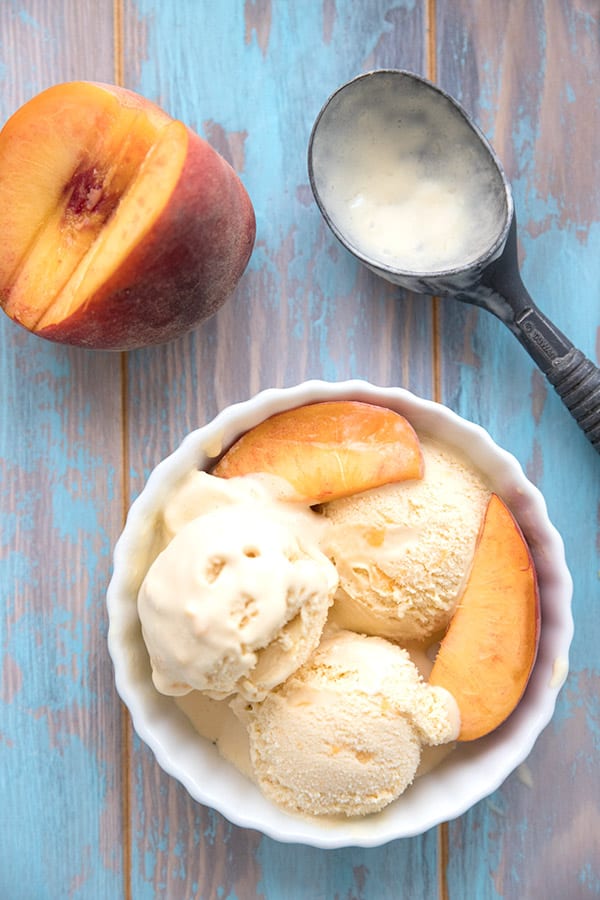 Top down photo of peach ice cream in a white bowl on a blue weathered table. 