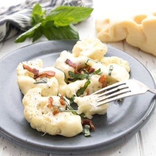 A grilled cauliflower steak topped with Jarlsberg cheese, bacon, and fresh basil
