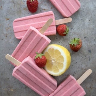 Five strawberry lemonade popsicles on a cookie sheet