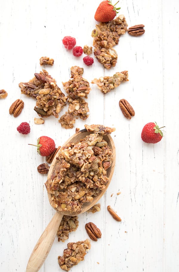 Top down photo of granola clusters in a wooden scoop on a white table