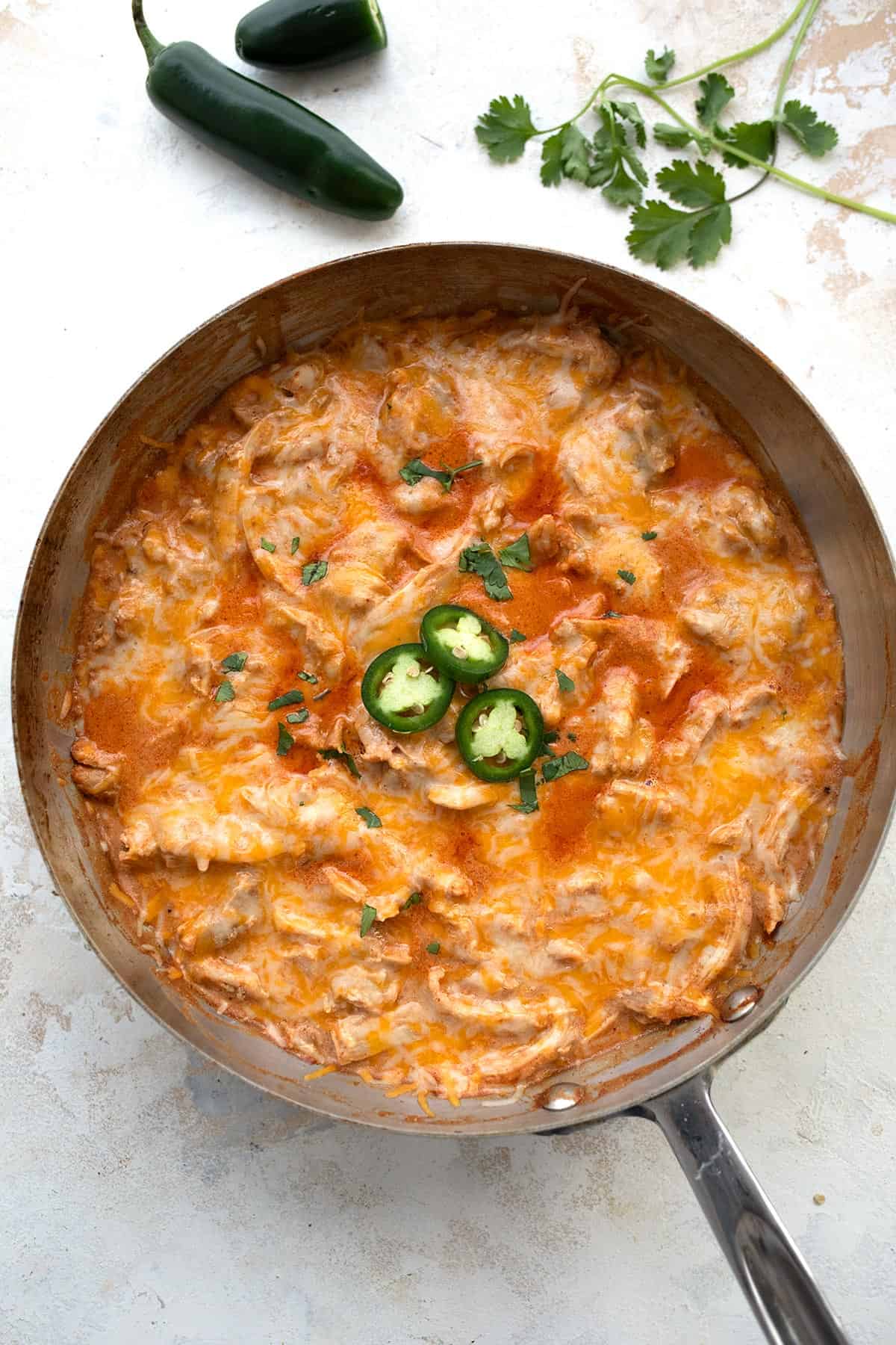 Top down image of Keto Enchilada Skillet in a metal pan, with jalapeño and cilantro above it. 