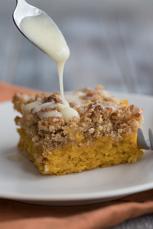 A slice of pumpkin crumb cake with vanilla glaze being drizzled over.