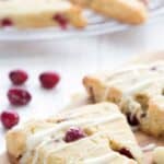 Titled image of Keto Cranberry Orange Scones on a wooden cutting board, with a drizzle of white chocolate.