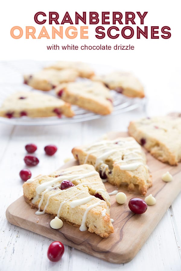 Keto cranberry orange scones with white chocolate drizzle on a wooden cutting board. 