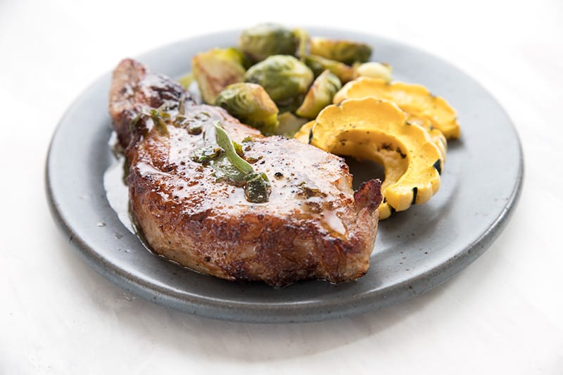 A keto pork chop on a grey plate with squash and Brussels sprouts.