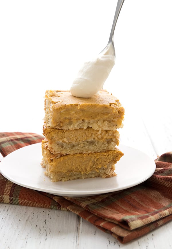 Putting whipped cream on a stack of keto pumpkin cake bars. 