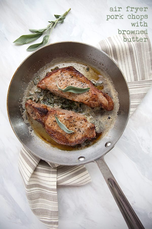 Perfectly browned air fryer pork chops in a brown butter sauce on a marble tabletop.