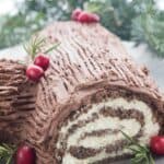 Titled image of a keto buche de noel in a pewter tray with evergreen branches in the background.