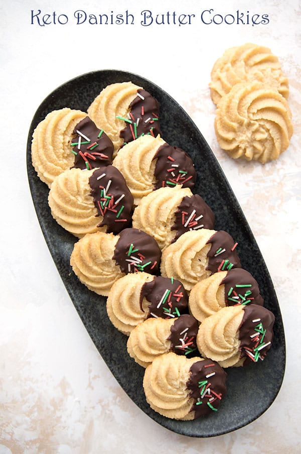 Low carb Danish Butter Cookies on a black platter. Dipped in chocolate with holiday sprinkles too. 